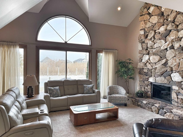 carpeted living room featuring a healthy amount of sunlight, high vaulted ceiling, and a stone fireplace