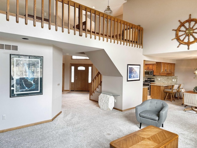 living area featuring light carpet, stairs, a towering ceiling, and baseboards