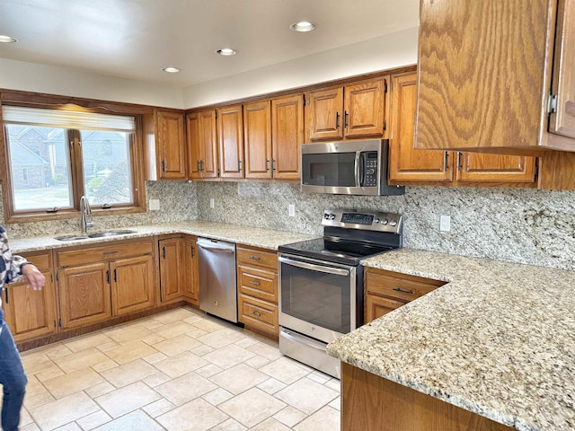 kitchen with decorative backsplash, brown cabinets, light stone countertops, stainless steel appliances, and a sink