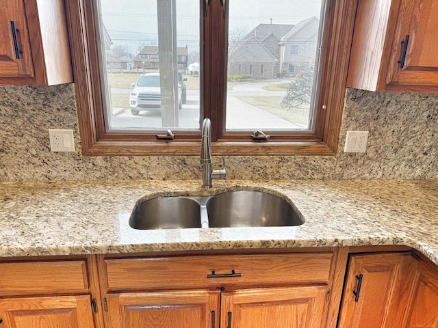 interior details featuring brown cabinetry, light stone counters, decorative backsplash, and a sink