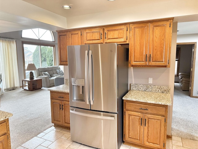 kitchen with stone tile floors, stainless steel refrigerator with ice dispenser, brown cabinets, and light colored carpet