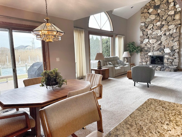 dining area with a notable chandelier, high vaulted ceiling, a stone fireplace, and light colored carpet