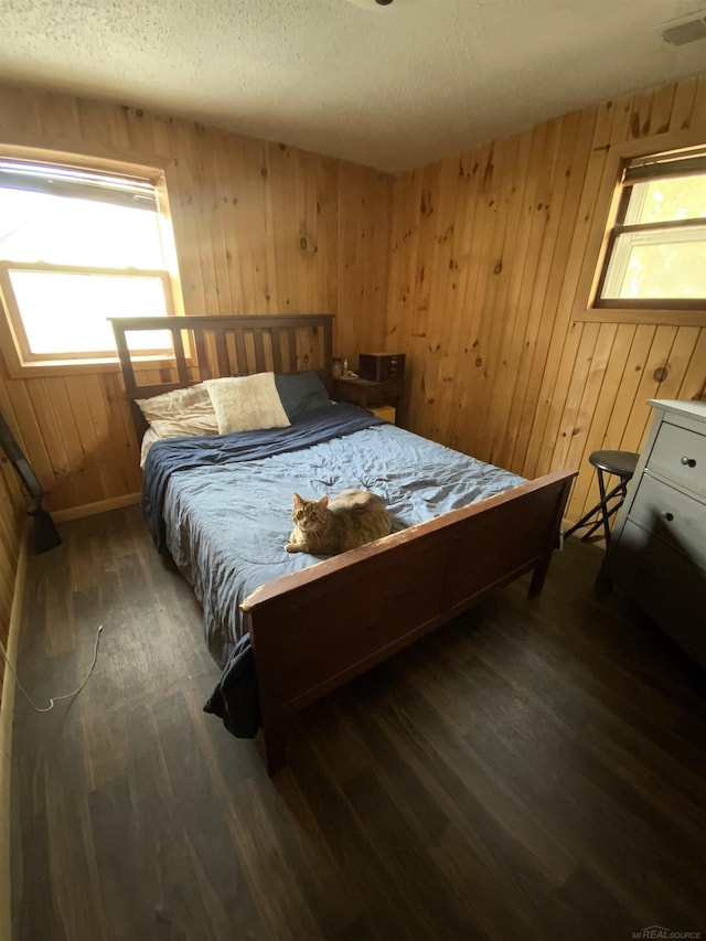 bedroom with a textured ceiling, wood finished floors, visible vents, and wooden walls