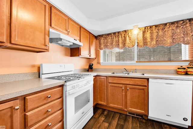 kitchen with under cabinet range hood, white appliances, a sink, light countertops, and dark wood-style floors