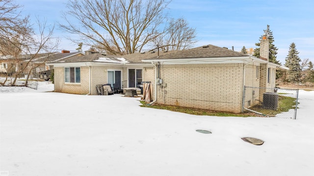 snow covered property featuring brick siding, a chimney, and central AC unit