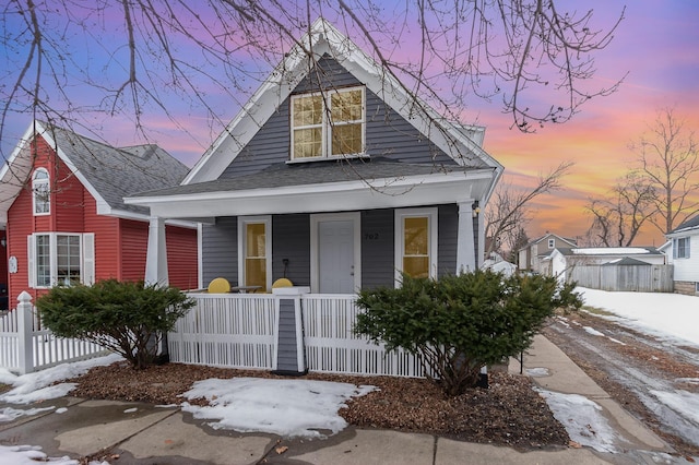 view of front of home with covered porch, a shingled roof, and fence