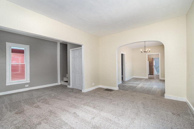 spare room featuring arched walkways, carpet, an inviting chandelier, baseboards, and stairs