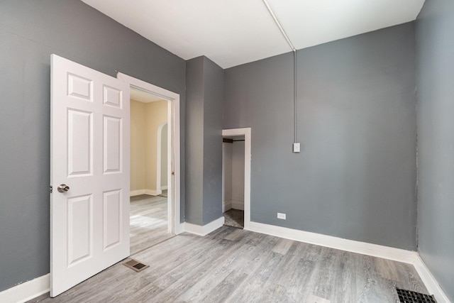 unfurnished bedroom featuring arched walkways, visible vents, light wood-style flooring, and baseboards