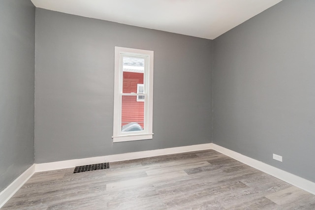 spare room featuring wood finished floors, visible vents, and baseboards