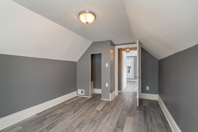 additional living space with baseboards, vaulted ceiling, visible vents, and dark wood finished floors