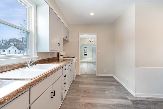 kitchen featuring arched walkways, gas range gas stove, light wood-style floors, a sink, and baseboards