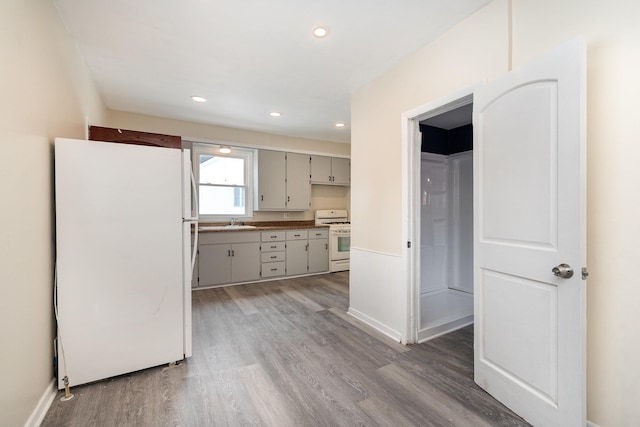 kitchen with white appliances, baseboards, light wood-type flooring, a sink, and recessed lighting