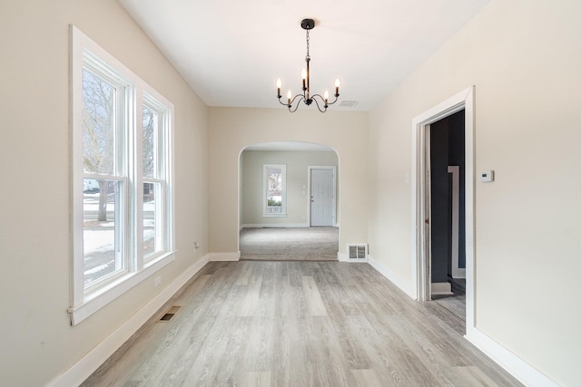 unfurnished dining area with light wood-style floors, arched walkways, visible vents, and an inviting chandelier