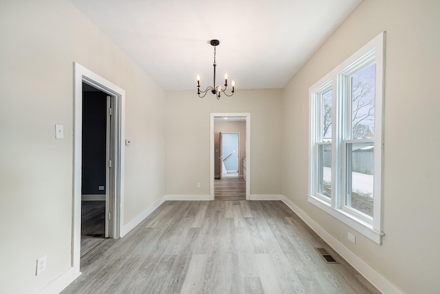 unfurnished dining area with light wood-type flooring, a notable chandelier, baseboards, and a wealth of natural light