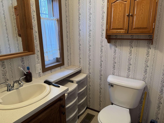 half bathroom featuring visible vents, toilet, wallpapered walls, and vanity