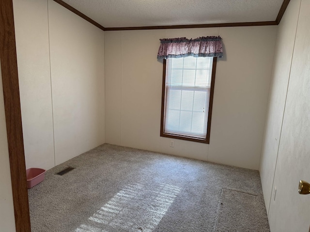 carpeted spare room featuring visible vents, a textured ceiling, and ornamental molding