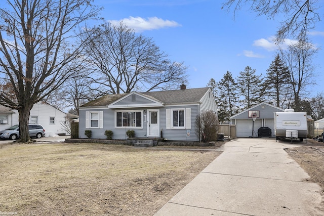 bungalow-style house featuring a shingled roof, an outbuilding, a detached garage, and a chimney