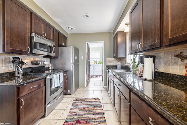 kitchen with light tile patterned floors, dark brown cabinetry, a sink, appliances with stainless steel finishes, and dark stone counters