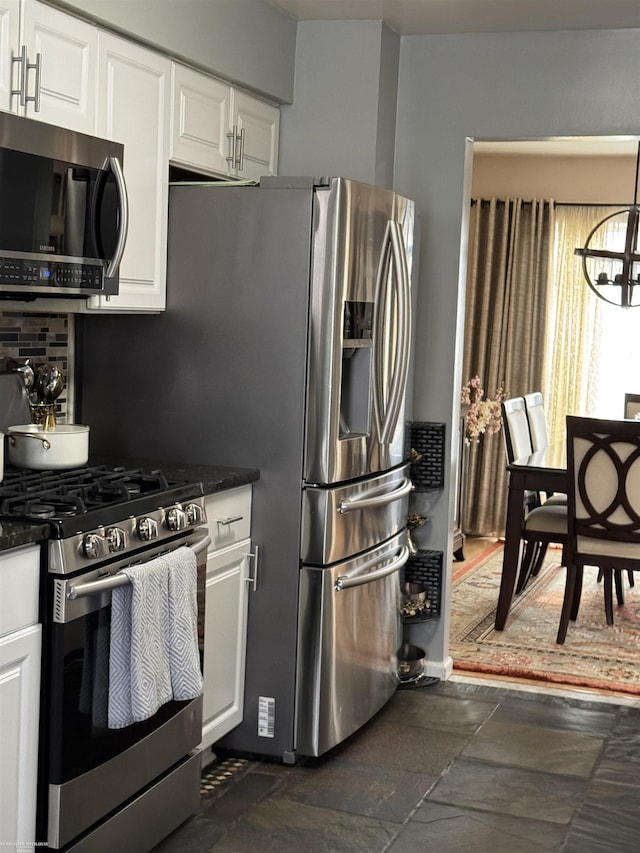 kitchen featuring tasteful backsplash, stone tile floors, appliances with stainless steel finishes, white cabinetry, and a notable chandelier