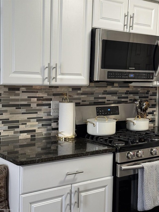 kitchen featuring appliances with stainless steel finishes, dark stone counters, white cabinetry, and decorative backsplash