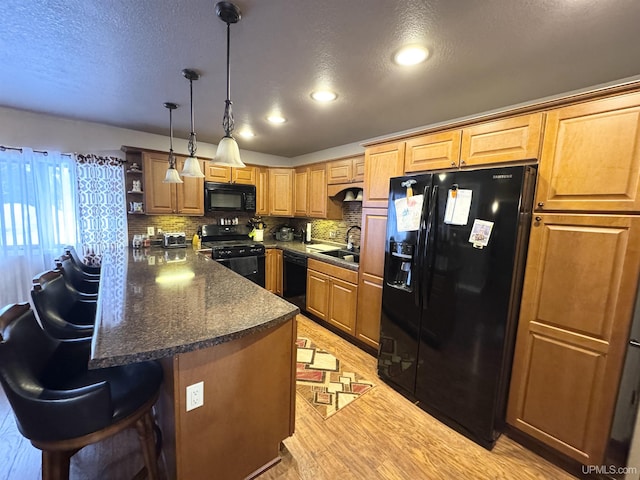 kitchen featuring a breakfast bar, a sink, black appliances, light wood finished floors, and tasteful backsplash