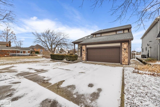 snow covered property with stone siding and an attached garage