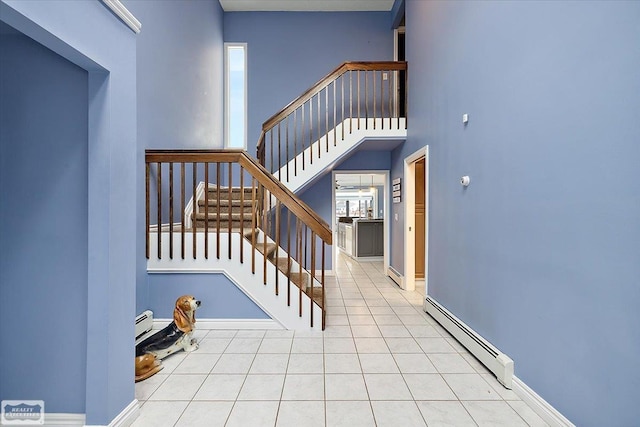 stairway with a baseboard radiator, tile patterned flooring, a towering ceiling, and baseboards