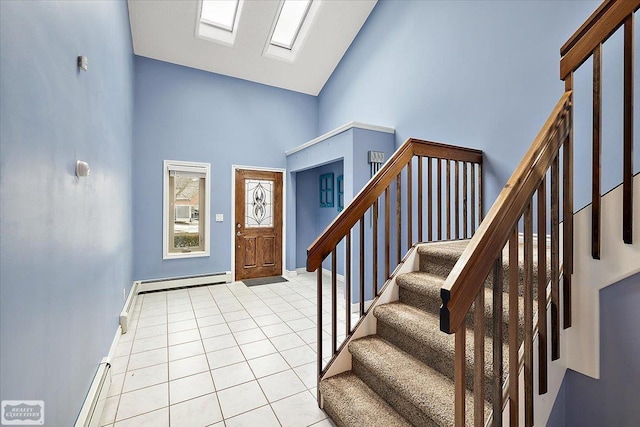 entryway with high vaulted ceiling, a baseboard radiator, light tile patterned flooring, a skylight, and stairway