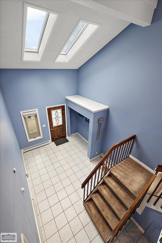 entryway featuring lofted ceiling with skylight, stairway, a textured ceiling, and light tile patterned floors