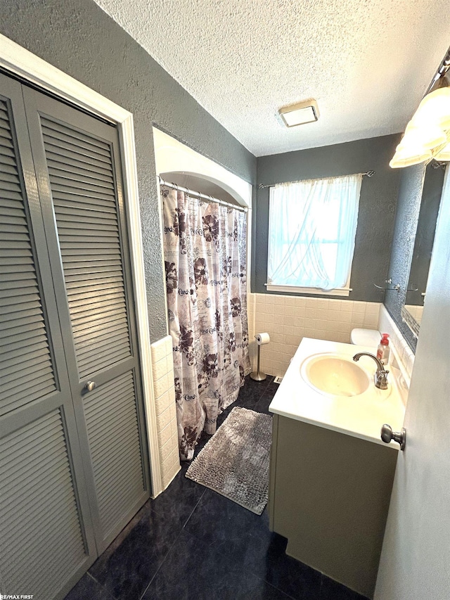 full bath with a closet, a textured ceiling, tile walls, and a textured wall