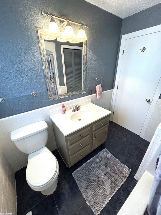 full bath with a wainscoted wall, tile walls, tile patterned flooring, and a textured wall