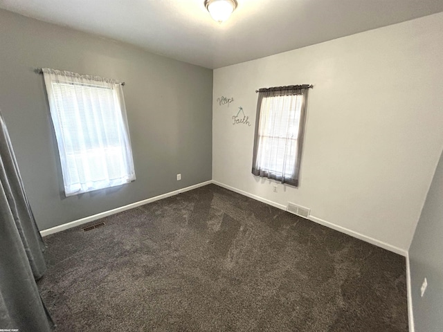 unfurnished room with dark colored carpet, visible vents, plenty of natural light, and baseboards