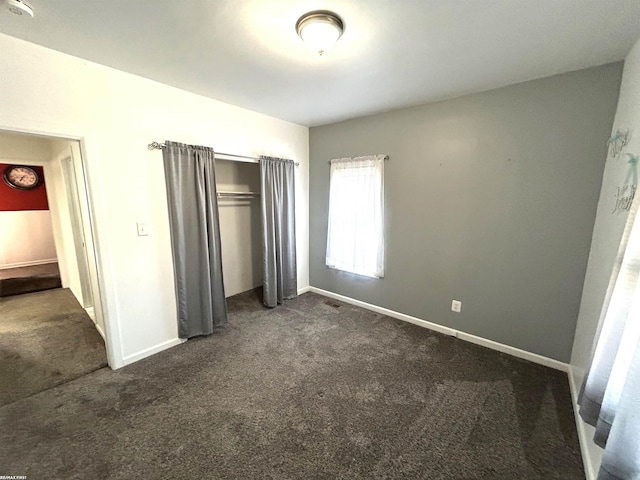 unfurnished bedroom with dark colored carpet, a closet, and baseboards