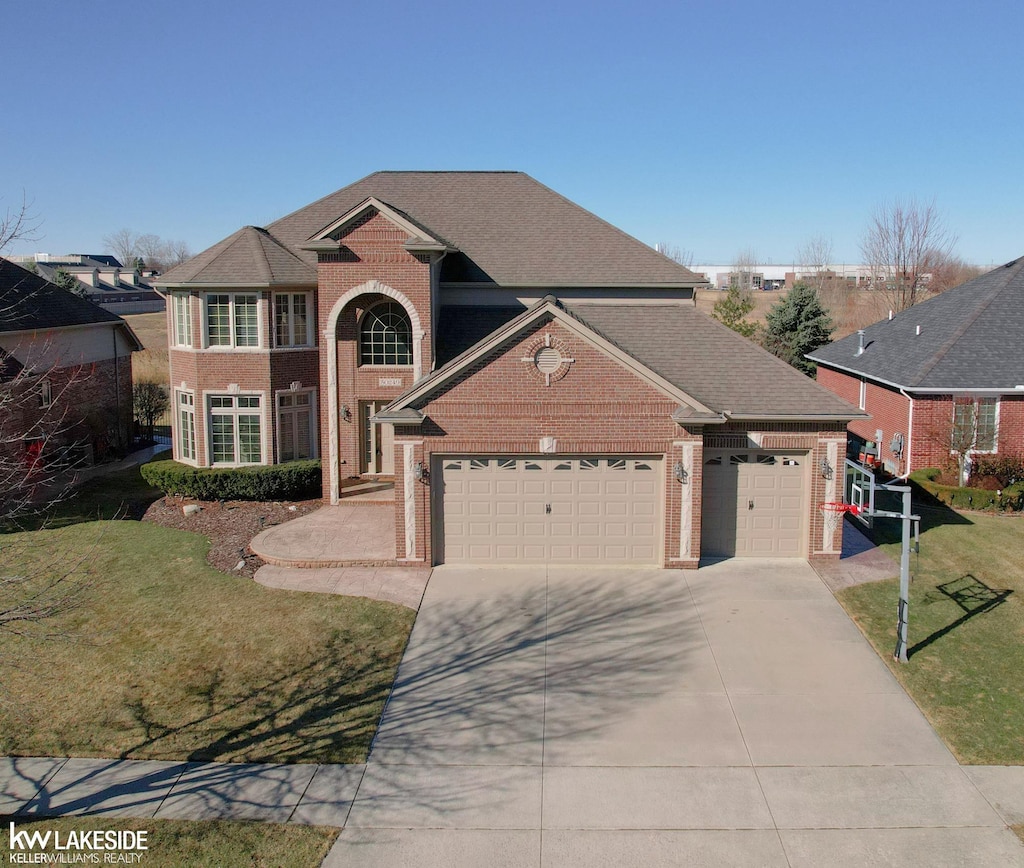 traditional-style house featuring brick siding, a shingled roof, a front yard, a garage, and driveway