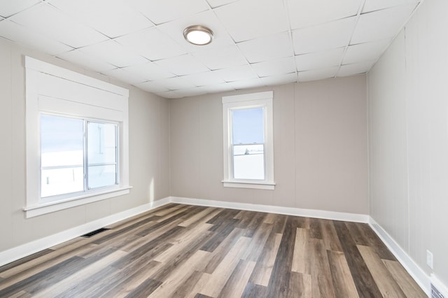 unfurnished room featuring a paneled ceiling, visible vents, baseboards, and wood finished floors