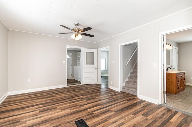 empty room featuring ceiling fan, dark wood-style flooring, a sink, baseboards, and stairs