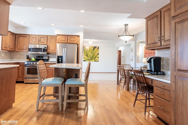 kitchen featuring brown cabinets, a center island, stainless steel appliances, light countertops, and light wood-style floors