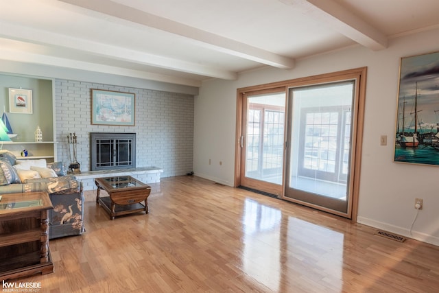 living area featuring baseboards, visible vents, light wood-type flooring, a brick fireplace, and beam ceiling