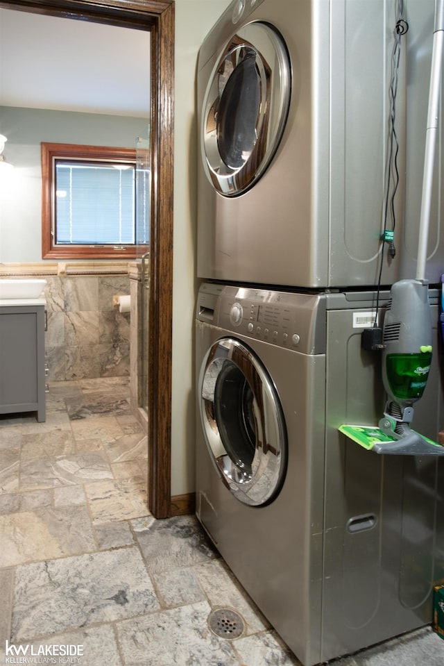 laundry area featuring laundry area, stone tile flooring, and stacked washer and clothes dryer