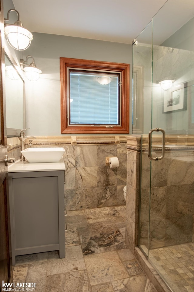 full bathroom with a stall shower, tile walls, vanity, and toilet