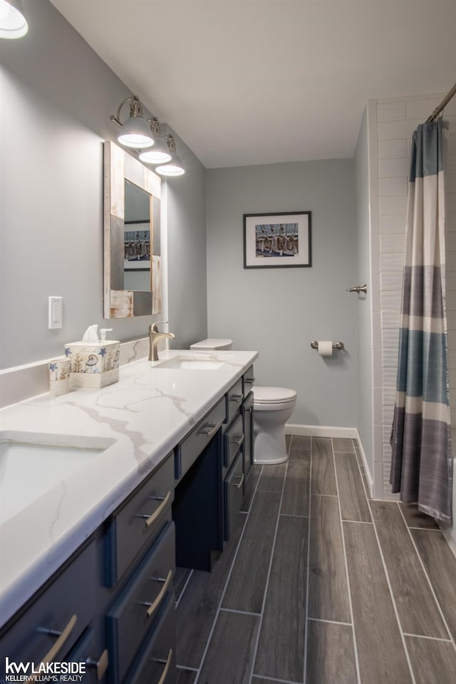 full bathroom with wood finish floors, double vanity, toilet, a sink, and baseboards