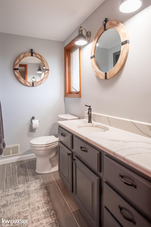 bathroom with toilet, wood finish floors, vanity, visible vents, and baseboards