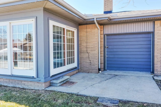 doorway to property with brick siding, a chimney, and an attached garage