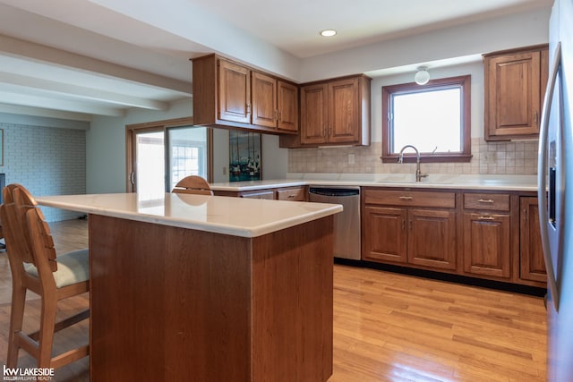 kitchen with brown cabinetry, a kitchen breakfast bar, stainless steel appliances, light wood-type flooring, and a sink