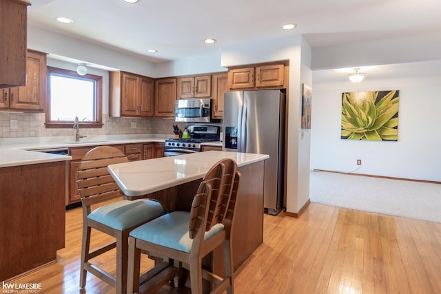 kitchen featuring a breakfast bar area, a sink, appliances with stainless steel finishes, brown cabinets, and decorative backsplash