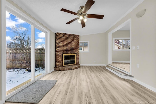 unfurnished living room with light wood-style flooring, a fireplace, crown molding, and a wealth of natural light