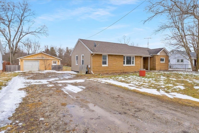 view of front of house featuring an outbuilding, brick siding, a detached garage, fence, and driveway