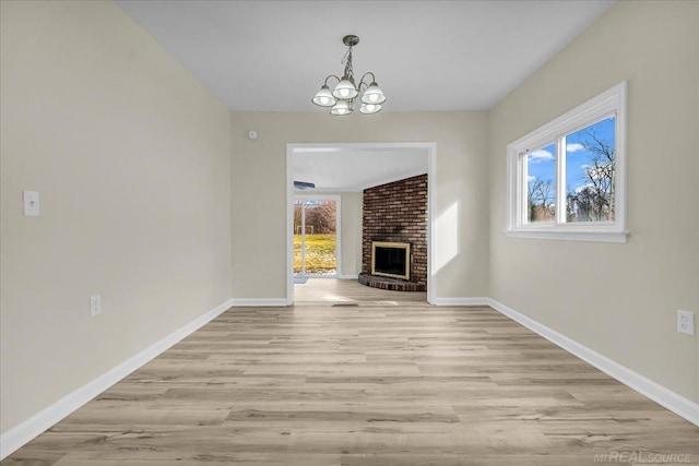 unfurnished living room with light wood-style flooring, a fireplace, baseboards, and a notable chandelier