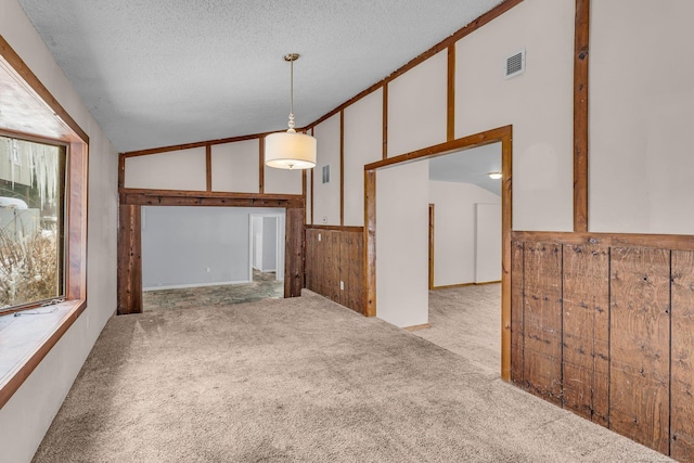 interior space featuring carpet, lofted ceiling, visible vents, wooden walls, and a textured ceiling