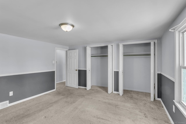 unfurnished bedroom with carpet floors, two closets, visible vents, and baseboards